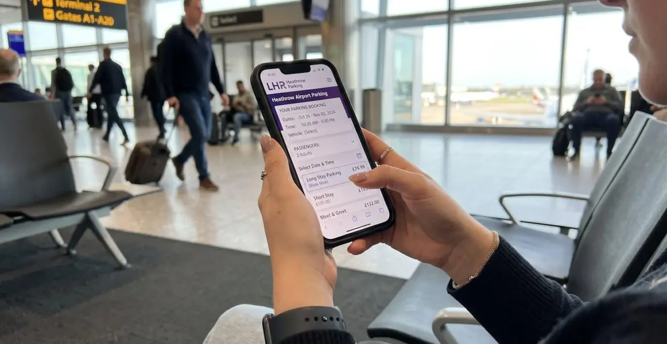 Gros plan sur des mains tenant un smartphone avec un écran de réservation complètement flouté, posé sur un bureau moderne et propre sous une lumière naturelle latérale