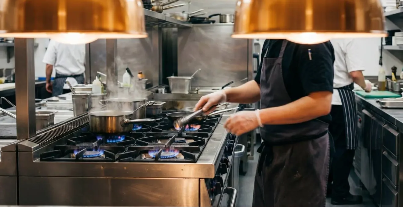 Chef professionnel travaillant sur des équipements de cuisson au gaz dans une cuisine de restaurant collectif
